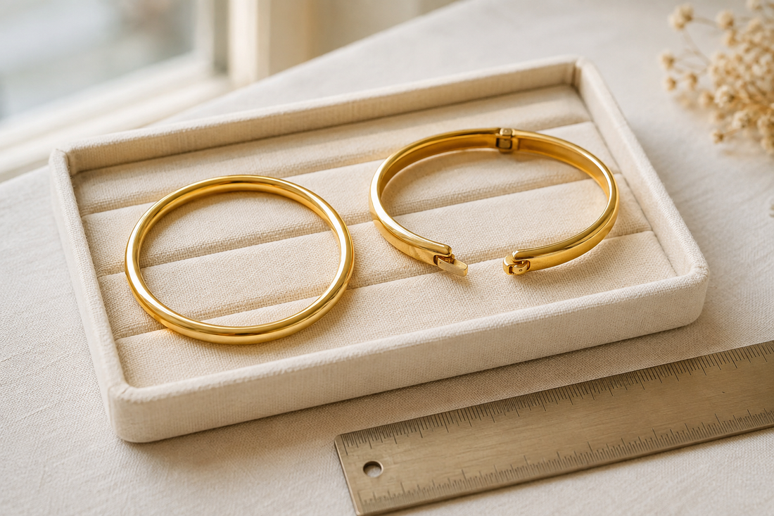 Round slip-on gold bangle and open hinged gold bangle on an ivory tray beside a ruler.