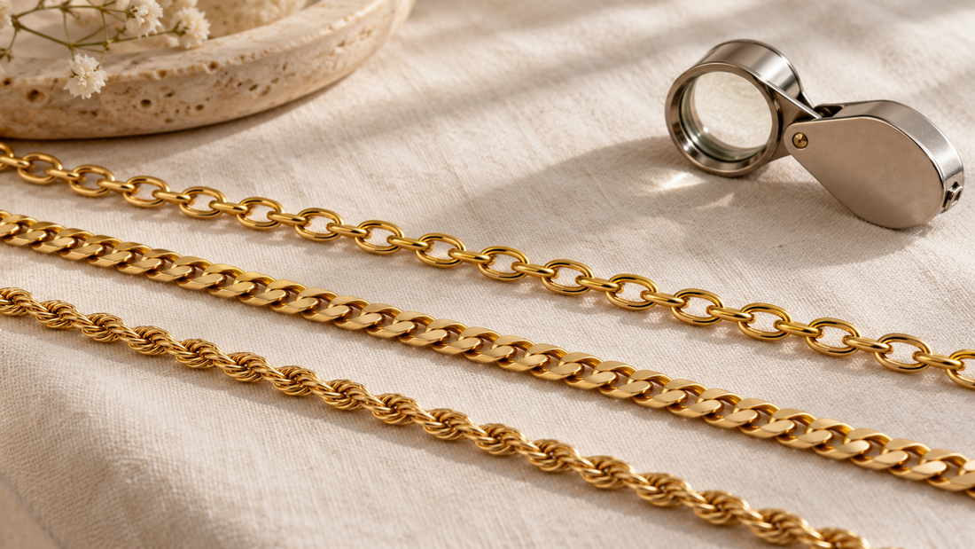 Three yellow-gold chains with oval cable, flat curb and twisted rope-style links on ivory linen beside a loupe.