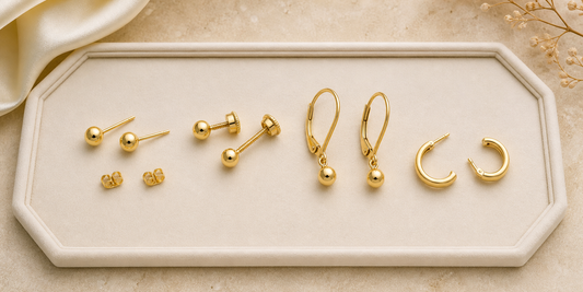 Gold stud, screw-back, lever-back and hinged hoop earrings on an ivory tray