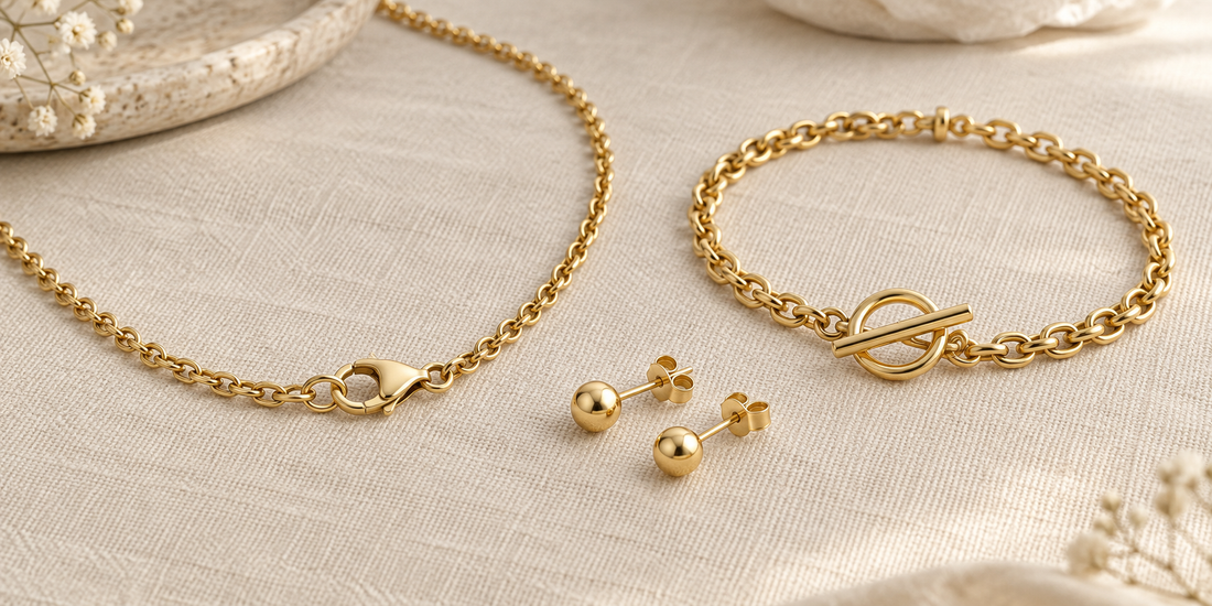 Gold chain with lobster clasp, bracelet with toggle fastening, and stud earrings with backs on ivory fabric.