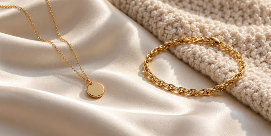 Yellow-gold pendant necklace and bracelet on ivory silk beside a textured knit fabric.