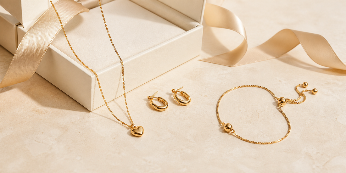 Gold pendant necklace, earrings and adjustable bracelet beside a cream gift box