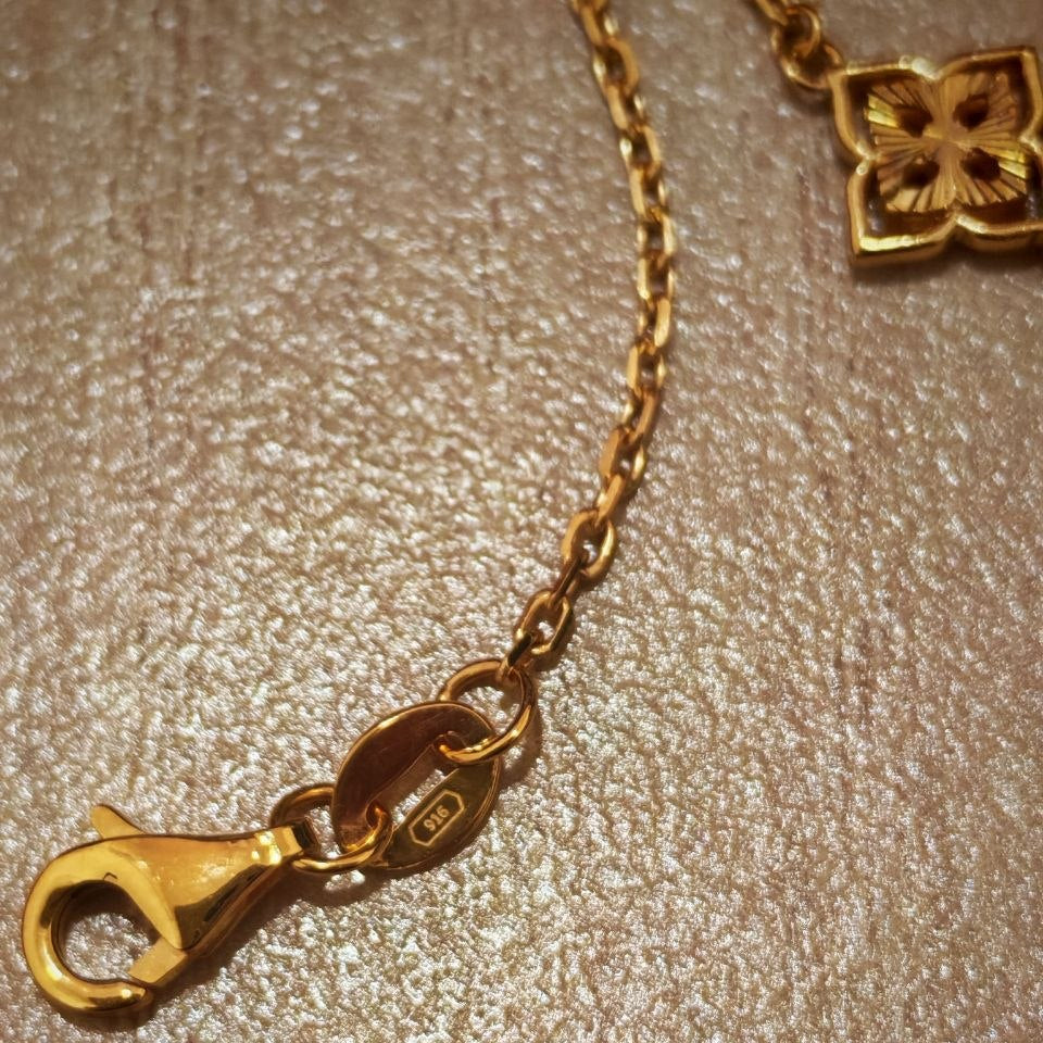 Close-up of a gold chain necklace with a lobster clasp and a small gold charm, resting on a textured beige surface.