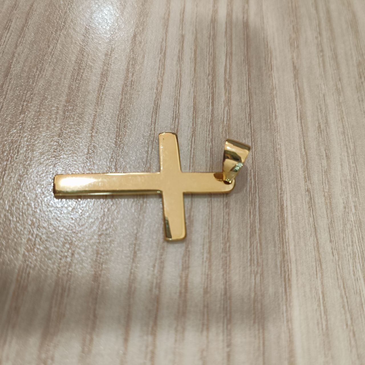 Gold cross pendant viewed from the opposite angle on a wood-grain surface