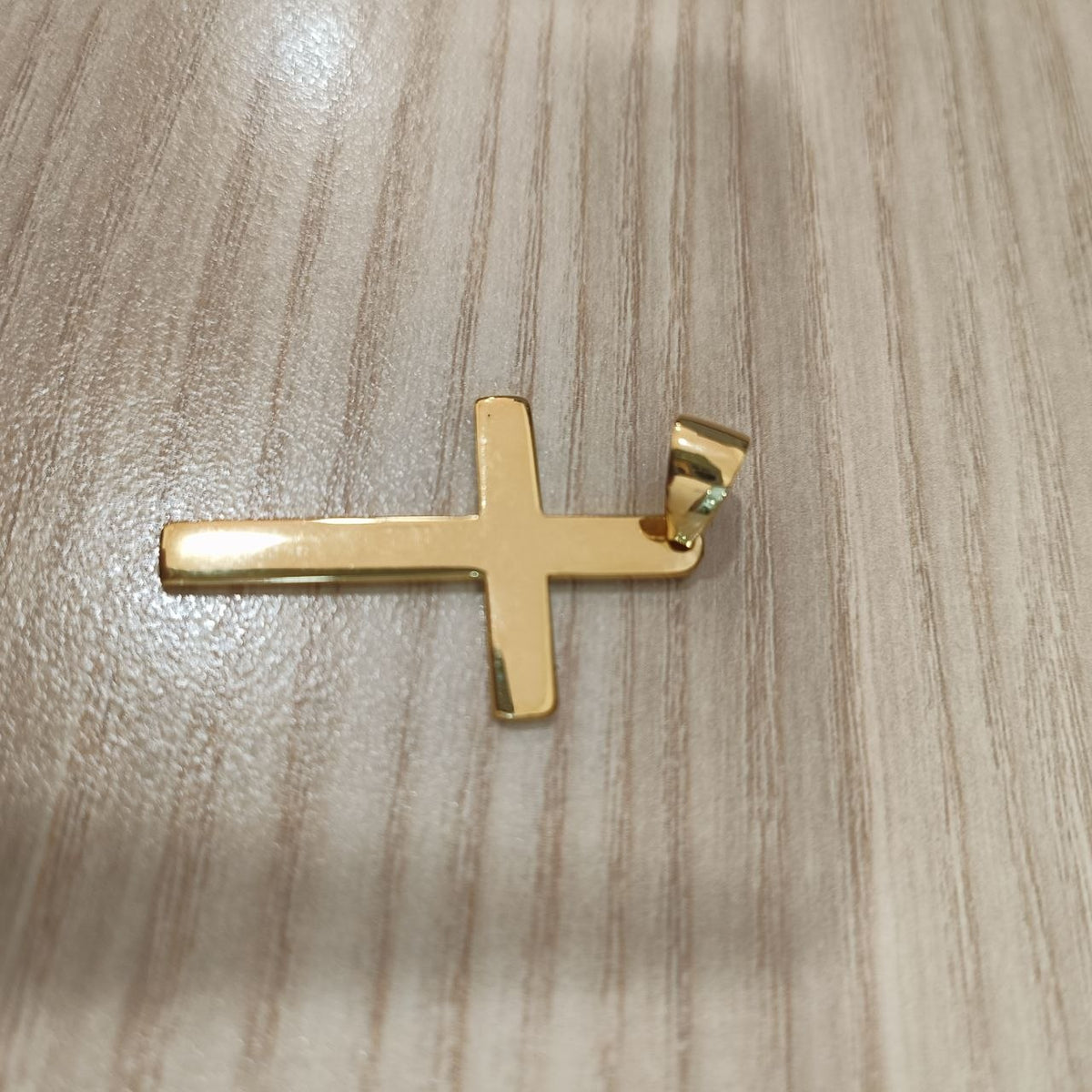 Gold cross pendant viewed from the opposite angle on a wood-grain surface