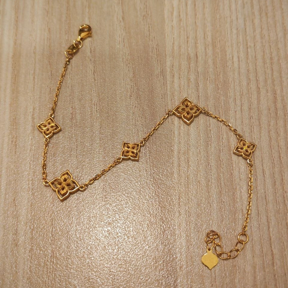 A delicate gold chain bracelet with five interlocking quatrefoil-shaped links, displayed on a light wood grain surface.